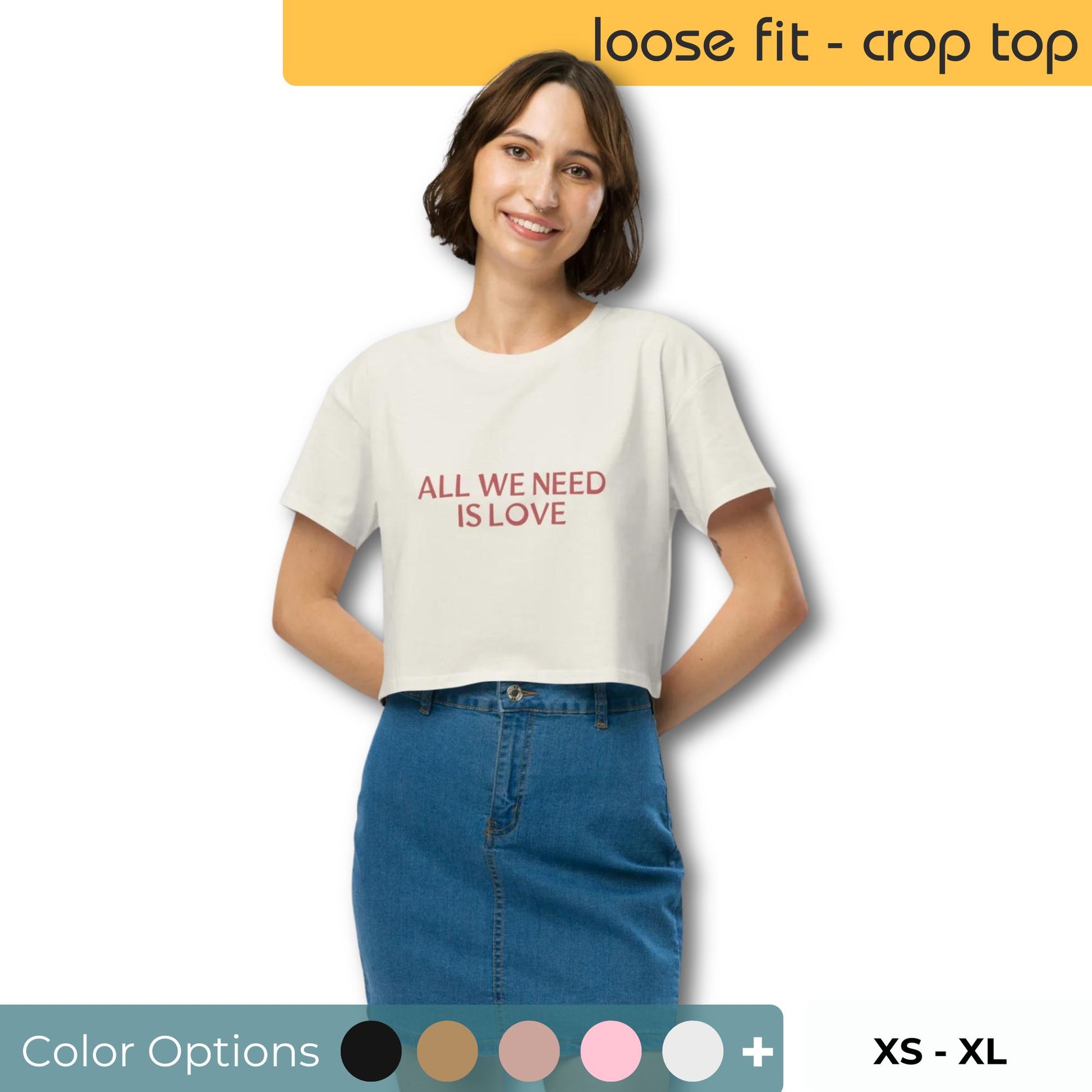 Woman smiling in a cream-colored crop top with "All We Need Is Love" print, available in multiple colors and sizes XS to XL.