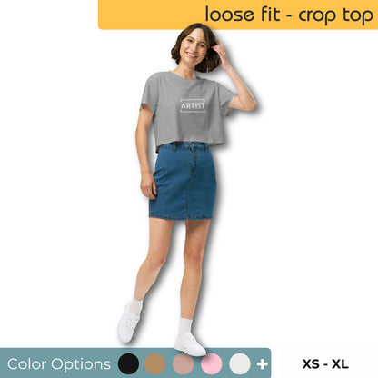 Smiling woman wearing a loose-fitting gray crop top with the word 'ARTIST' printed across the chest, paired with a blue denim skirt, white sneakers, and displayed with a range of color options and sizes from XS to XL.