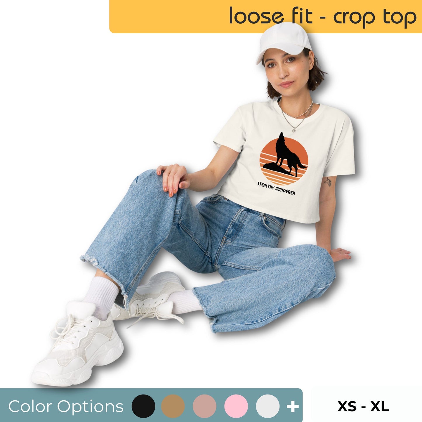 Fashionable woman in a white loose-fit crop top with a bold black silhouette and sunset graphic, paired with baggy blue jeans, white sneakers, and a white cap, including color options and size range XS to XL.