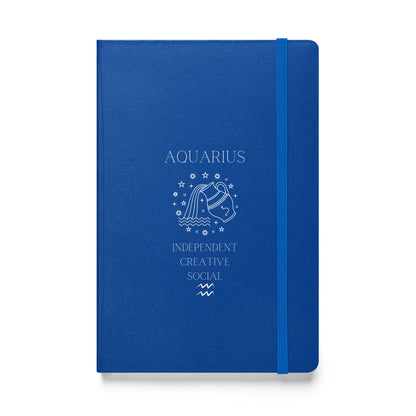 A blue hardcover notebook with 'AQUARIUS' and symbolic illustrations printed in white, along with the words 'INDEPENDENT CREATIVE SOCIAL'. The notebook features an elastic closure.