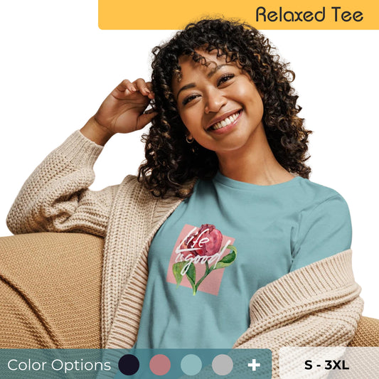 Cheerful woman with curly hair smiling and wearing a relaxed fit teal tee with 'Life in Bloom' floral graphic design, available in multiple color options, sizes S-3XL