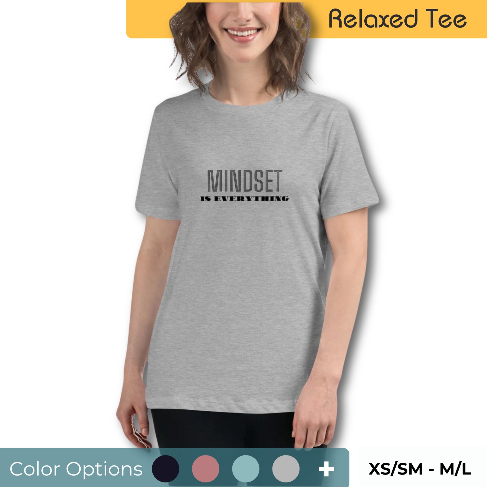 Smiling woman with short wavy hair wearing a relaxed fit light grey tee with 'Mindset is Everything' printed in black, available in multiple colors, sizes XS/SM to M/L.