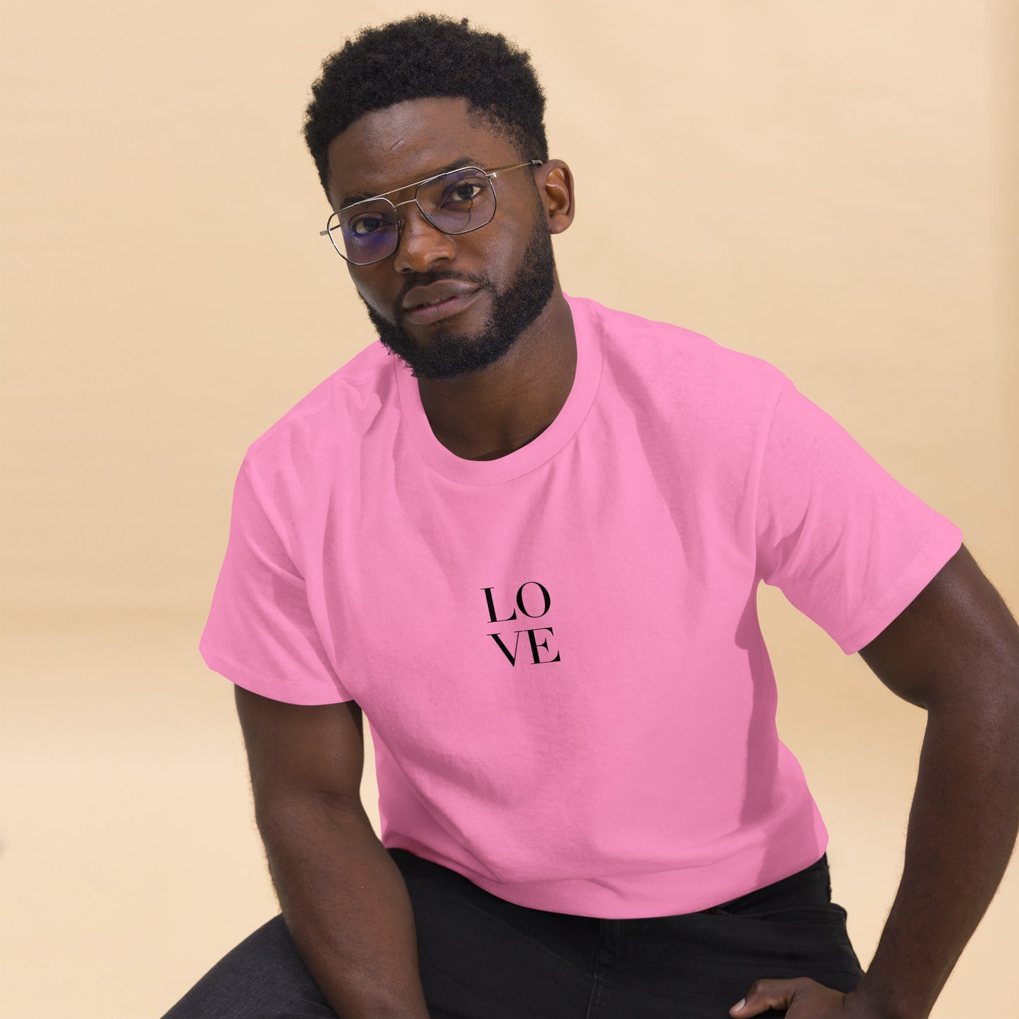 Man in pink t-shirt with "LOVE" print leaning forward against a light background, portraying casual style and positive messaging.