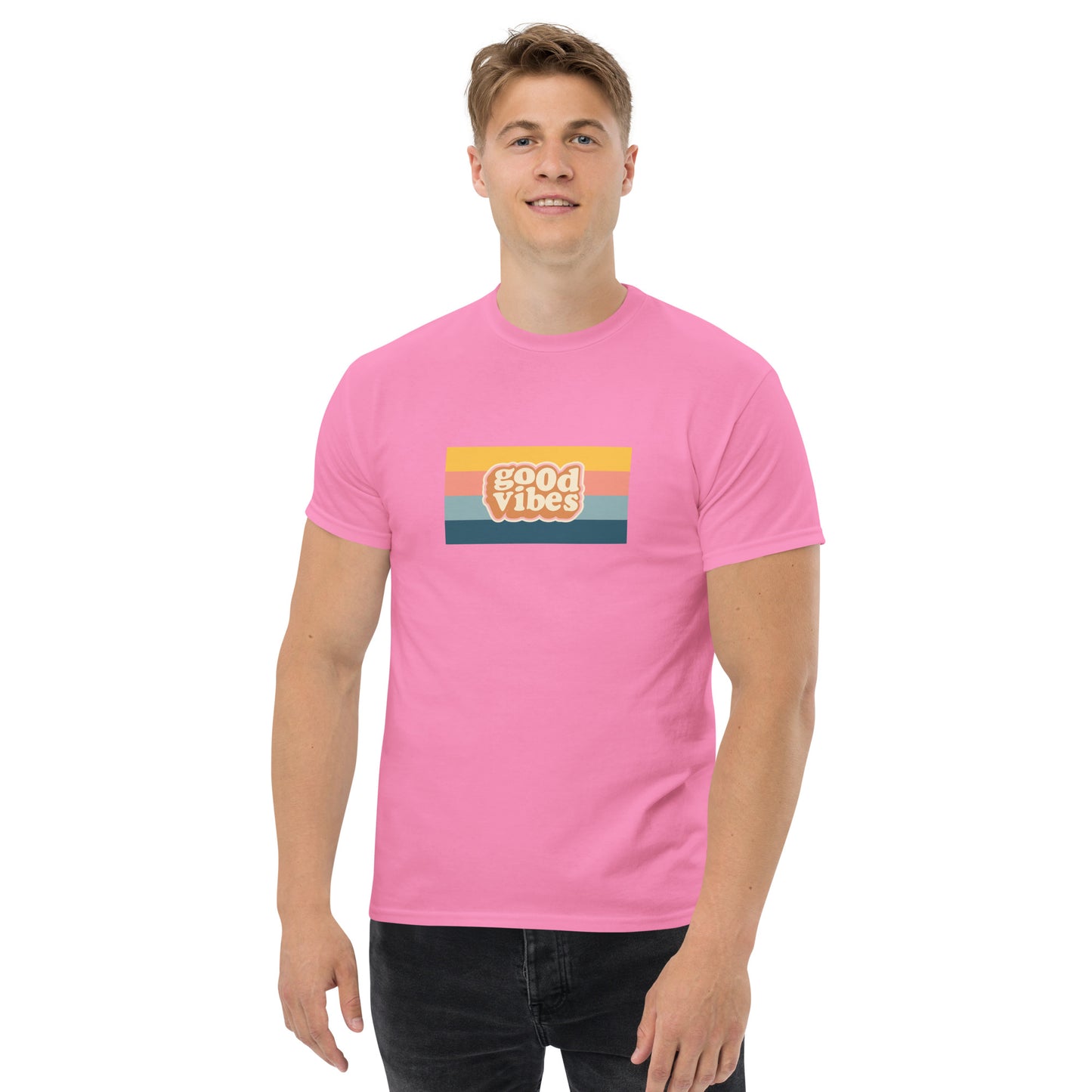 Smiling man wearing a pink classic tee with a colorful 'good vibes' retro graphic, symbolizing relaxed and inspirational personal style.