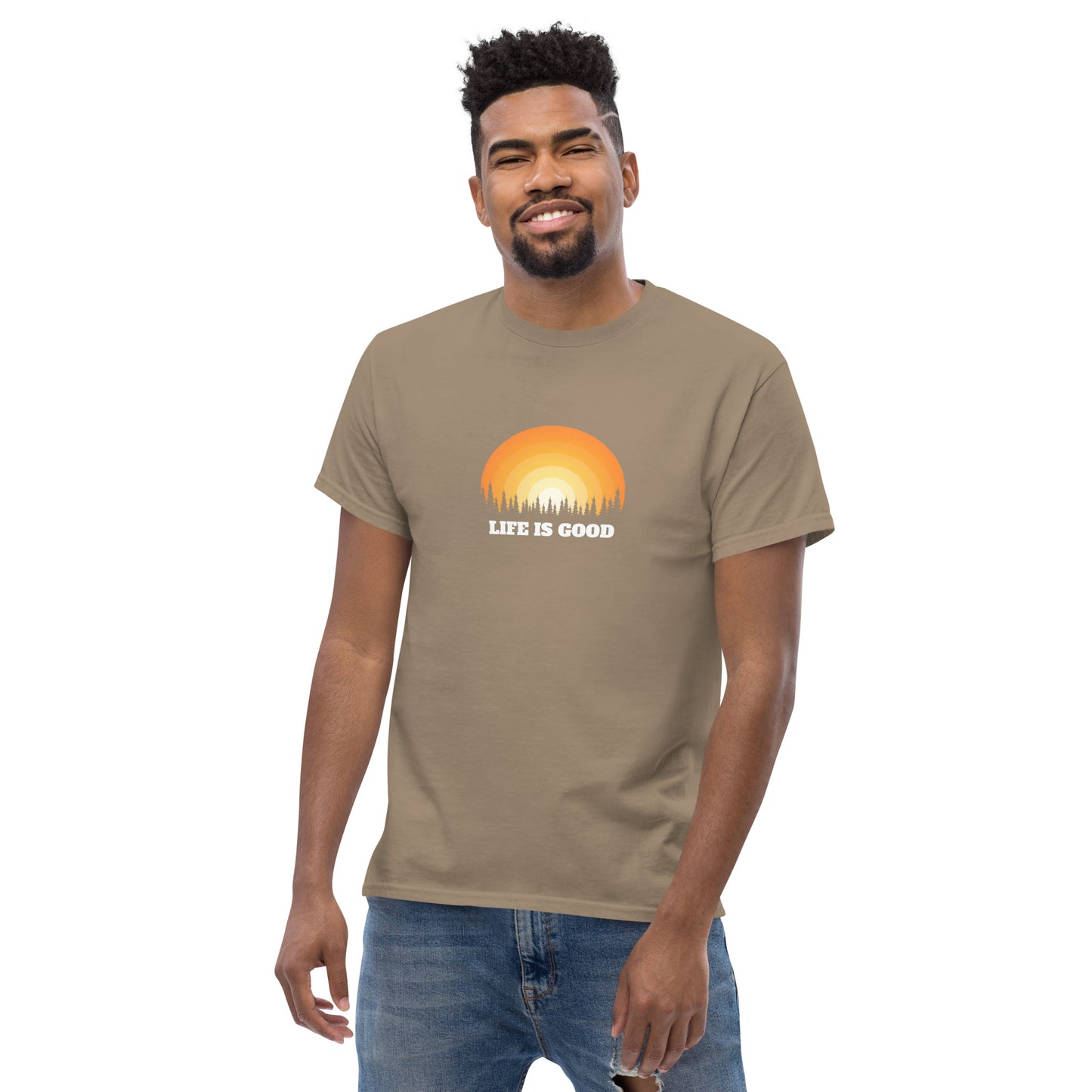 Happy man wearing a sand classic tee with a vibrant sunset graphic and 'Life Is Good' slogan, inspiring positivity and joy.