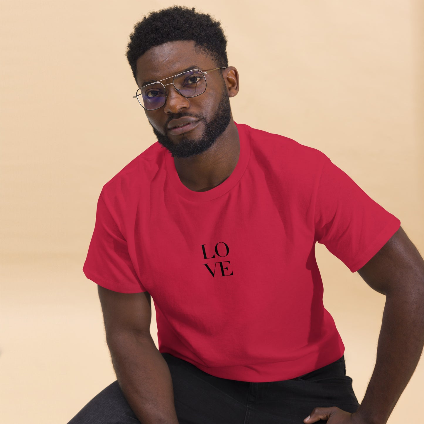 Man in cardinal red t-shirt with "LOVE" print leaning forward against a light background, portraying casual style and positive messaging.