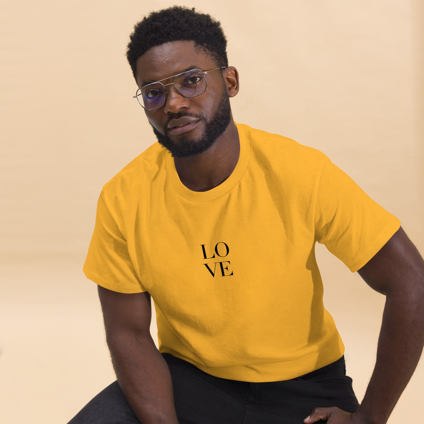 Man in yellow t-shirt with "LOVE" print leaning forward against a light background, portraying casual style and positive messaging.