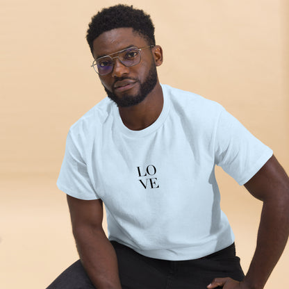 Man in white t-shirt with "LOVE" print leaning forward against a light background, portraying casual style and positive messaging.