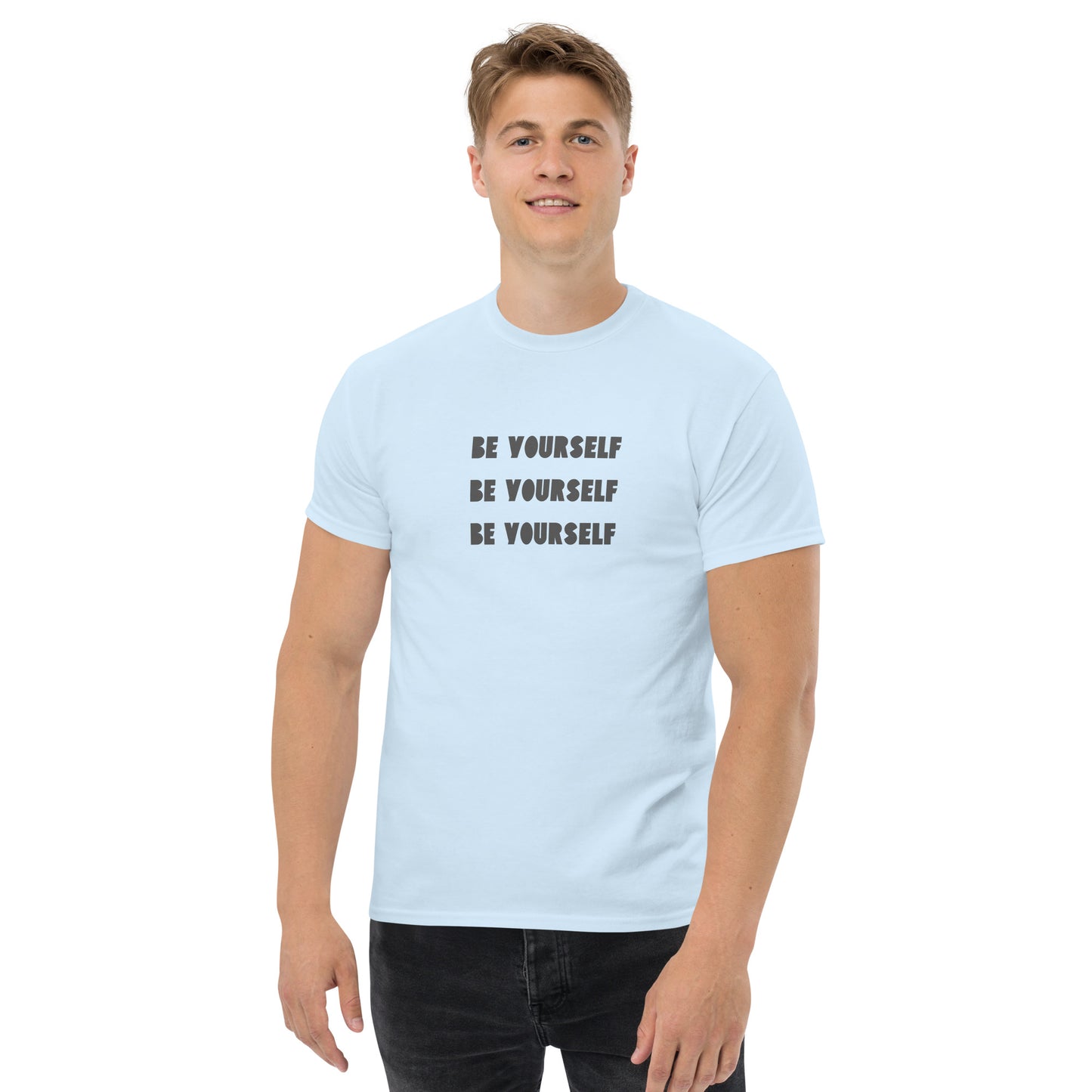 Smiling man in a light blue classic tee with 'BE YOURSELF' text fading vertically, echoing authenticity and personal expression.