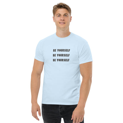 Smiling man in a light blue classic tee with 'BE YOURSELF' text fading vertically, echoing authenticity and personal expression.