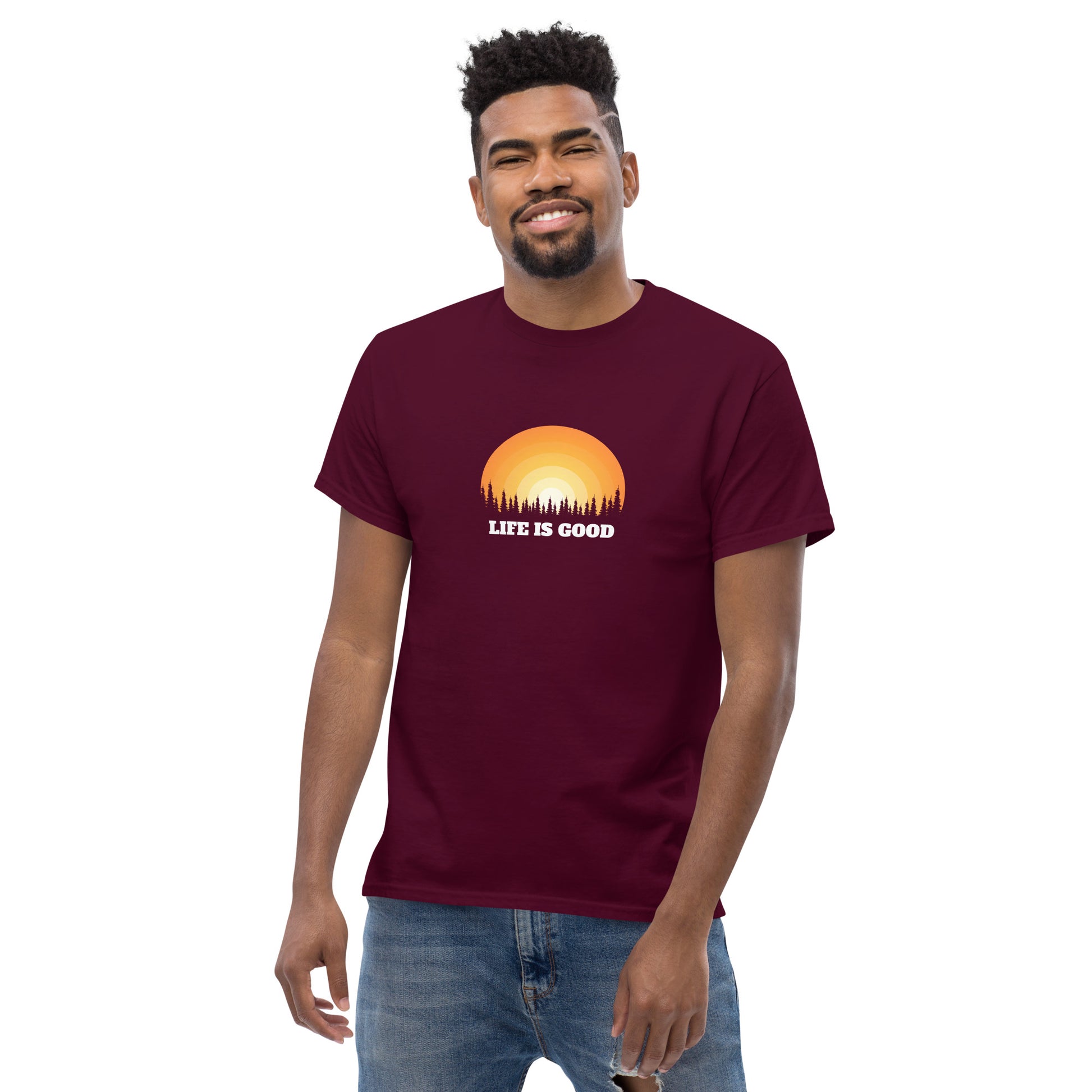 Happy man wearing a maroon classic tee with a vibrant sunset graphic and 'Life Is Good' slogan, inspiring positivity and joy.