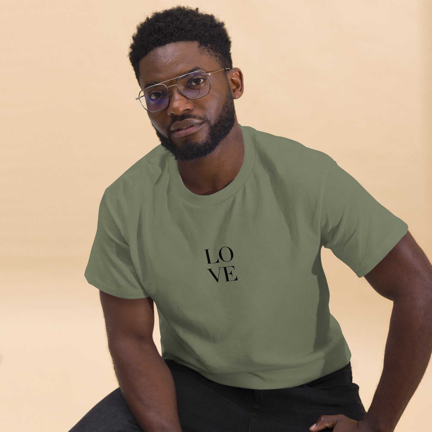 Man in military green t-shirt with "LOVE" print leaning forward against a light background, portraying casual style and positive messaging.