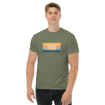 Smiling man wearing a military green classic tee with a colorful 'good vibes' retro graphic, symbolizing relaxed and inspirational personal style.