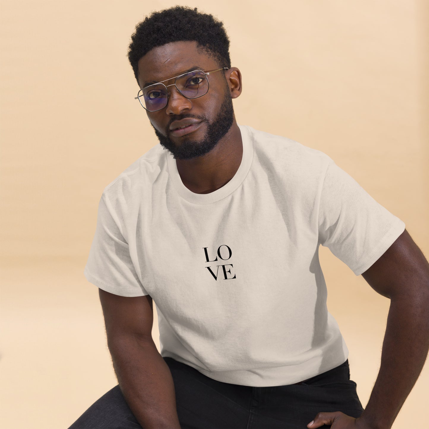 Man in sand t-shirt with "LOVE" print leaning forward against a light background, portraying casual style and positive messaging.