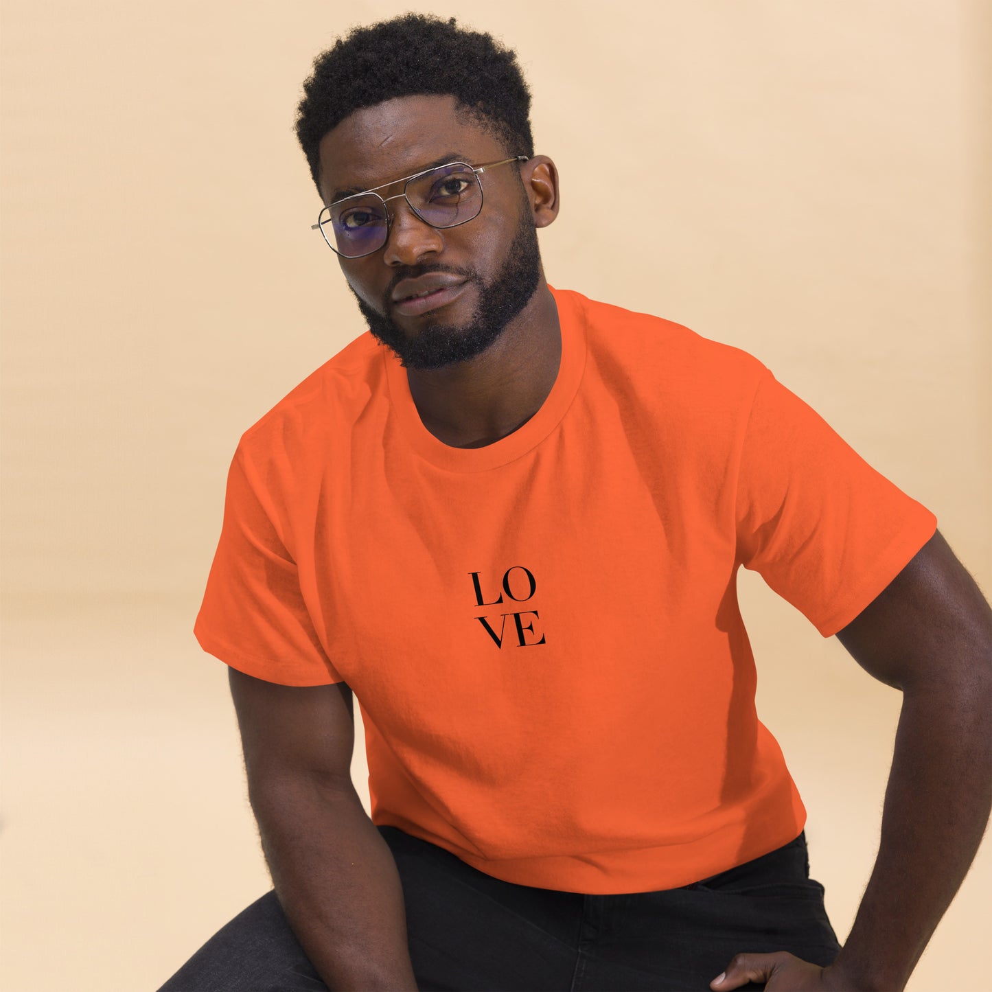 Man in orange t-shirt with "LOVE" print leaning forward against a light background, portraying casual style and positive messaging.