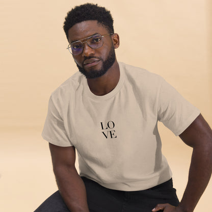 Man in sand t-shirt with "LOVE" print leaning forward against a light background, portraying casual style and positive messaging.