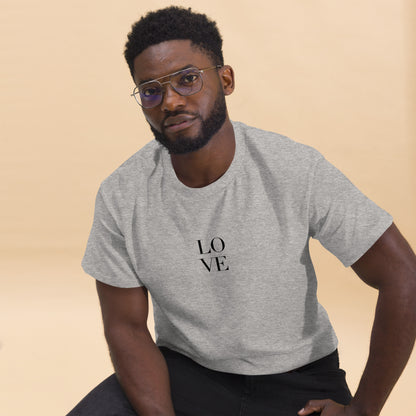 Man in grey t-shirt with "LOVE" print leaning forward against a light background, portraying casual style and positive messaging.