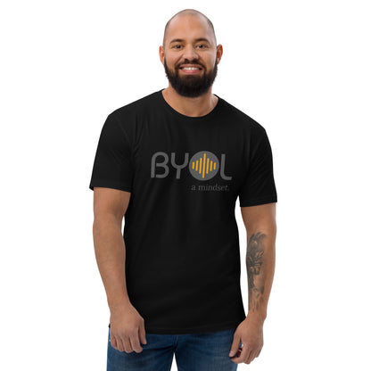 A bearded man with a shaved head wearing a black "BYOL: a mindset" T-shirt, smiling and standing with his arms at his sides. The T-shirt features the "BYOL" logo in gray and yellow on the front and is available in multiple colors (red, blue, gray, white, plus more) and sizes (S-3XL). The "be you out loud" logo is displayed at the top.