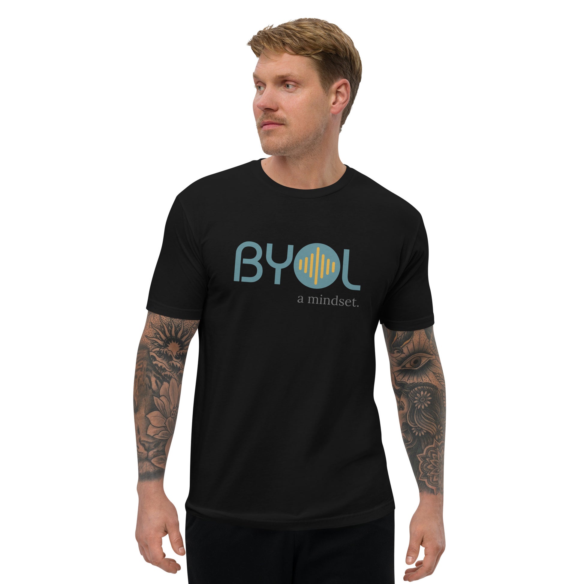 A young man with short blonde hair and arm tattoos wearing a black "BYOL: a mindset" T-shirt, standing and looking to the side. The T-shirt features the "BYOL" logo in teal and yellow on the front and is available in multiple colors (red, blue, gray, white, plus more) and sizes (S-3XL). The "be you out loud" logo is displayed at the top.