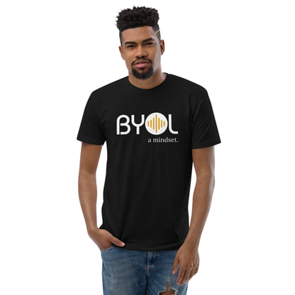 A young man with short curly hair wearing a black "BYOL: a mindset" T-shirt, standing with one hand in his pocket. The T-shirt features the "BYOL" logo in white and yellow on the front and is available in multiple colors (red, blue, gray, white, plus more) and sizes (S-3XL). The "be you out loud" logo is displayed at the top.