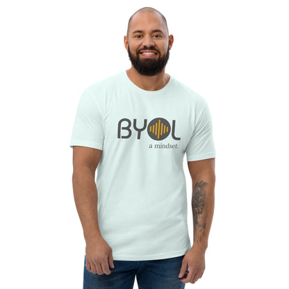 A bearded man with a shaved head wearing a light blue "BYOL: a mindset" T-shirt, smiling and standing with his arms at his sides. The T-shirt features the "BYOL" logo in gray and yellow on the front and is available in multiple colors (red, blue, gray, white, plus more) and sizes (S-3XL). The "be you out loud" logo is displayed at the top.