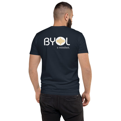 A young man with short dark hair and a beard wearing a navy blue "BYOL: a mindset" T-shirt, viewed from the back. The T-shirt features the "BYOL" logo in white and yellow on the back and is available in multiple colors (red, blue, gray, white, plus more) and sizes (S-3XL). The "be you out loud" logo is displayed at the top.