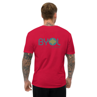 A young man with short blonde hair and arm tattoos wearing a red "BYOL: a mindset" T-shirt, viewed from the back. The T-shirt features the "BYOL" logo in teal and yellow on the back and is available in multiple colors (red, blue, gray, white, plus more) and sizes (S-3XL). The "be you out loud" logo is displayed at the top.