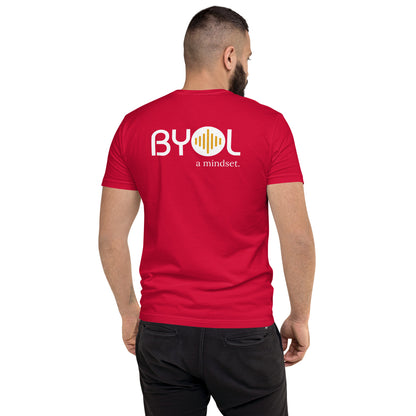 A young man with short dark hair and a beard wearing a cardinal red "BYOL: a mindset" T-shirt, viewed from the back. The T-shirt features the "BYOL" logo in white and yellow on the back and is available in multiple colors (red, blue, gray, white, plus more) and sizes (S-3XL). The "be you out loud" logo is displayed at the top.