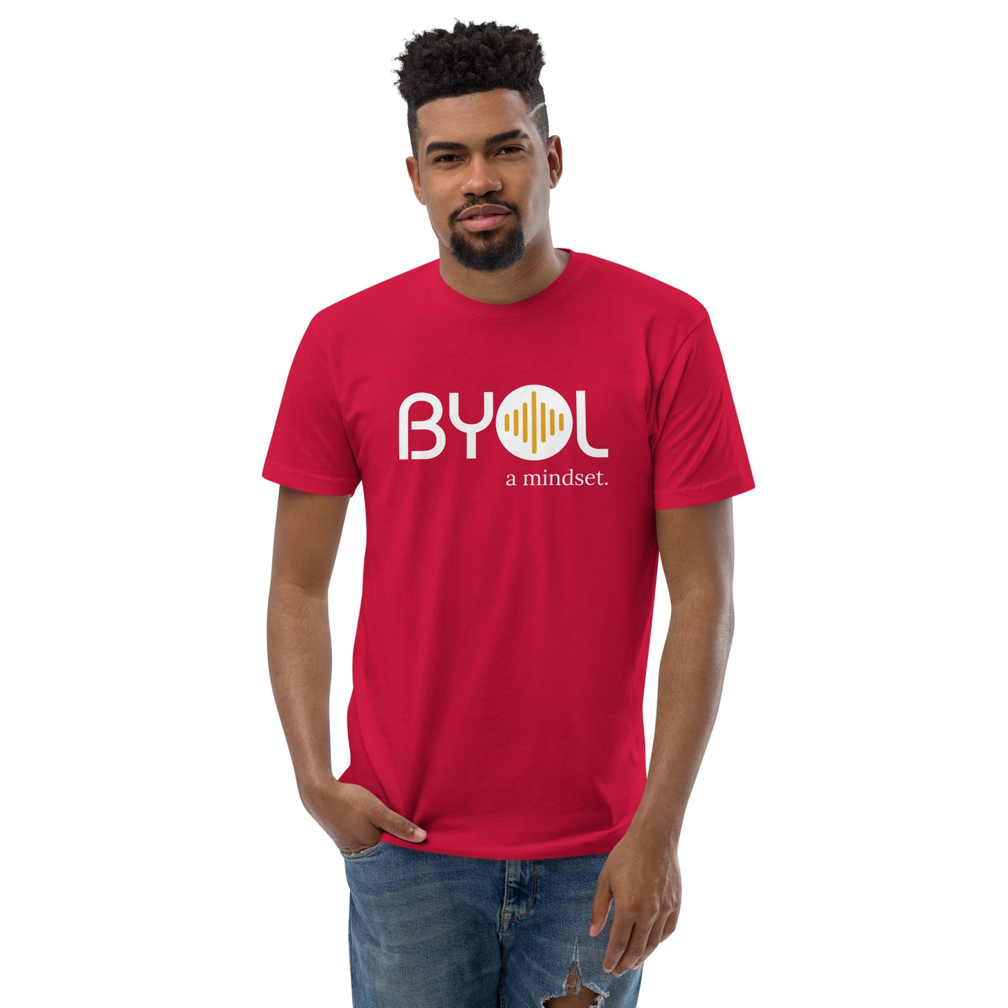 A young man with short curly hair wearing a red "BYOL: a mindset" T-shirt, standing with one hand in his pocket. The T-shirt features the "BYOL" logo in white and yellow on the front and is available in multiple colors (red, blue, gray, white, plus more) and sizes (S-3XL). The "be you out loud" logo is displayed at the top.