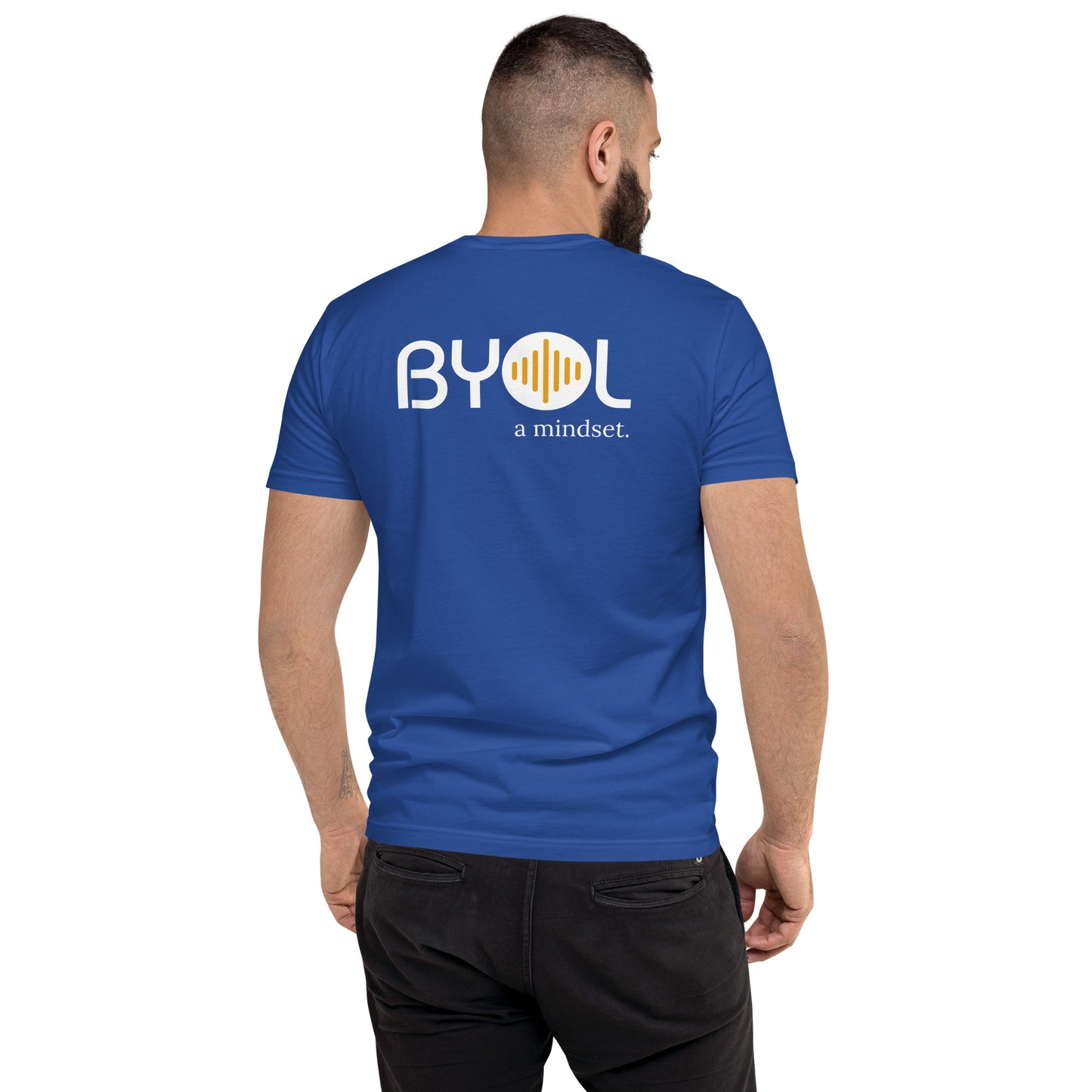 A young man with short dark hair and a beard wearing a royal blue "BYOL: a mindset" T-shirt, viewed from the back. The T-shirt features the "BYOL" logo in white and yellow on the back and is available in multiple colors (red, blue, gray, white, plus more) and sizes (S-3XL). The "be you out loud" logo is displayed at the top.