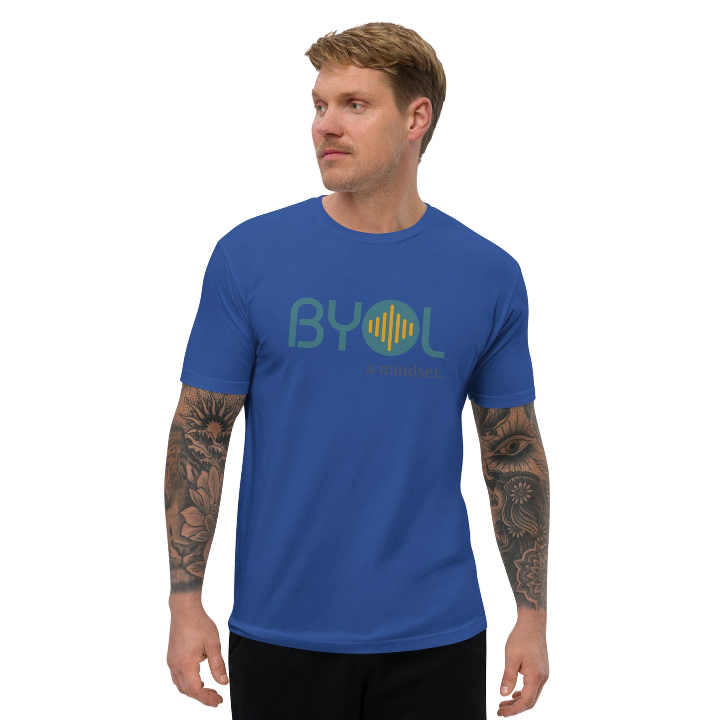 A young man with short blonde hair and arm tattoos wearing a royal blue "BYOL: a mindset" T-shirt, standing and looking to the side. The T-shirt features the "BYOL" logo in teal and yellow on the front and is available in multiple colors (red, blue, gray, white, plus more) and sizes (S-3XL). The "be you out loud" logo is displayed at the top.