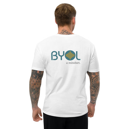 A young man with short blonde hair and arm tattoos wearing a white "BYOL: a mindset" T-shirt, viewed from the back. The T-shirt features the "BYOL" logo in teal and yellow on the back and is available in multiple colors (red, blue, gray, white, plus more) and sizes (S-3XL). The "be you out loud" logo is displayed at the top.