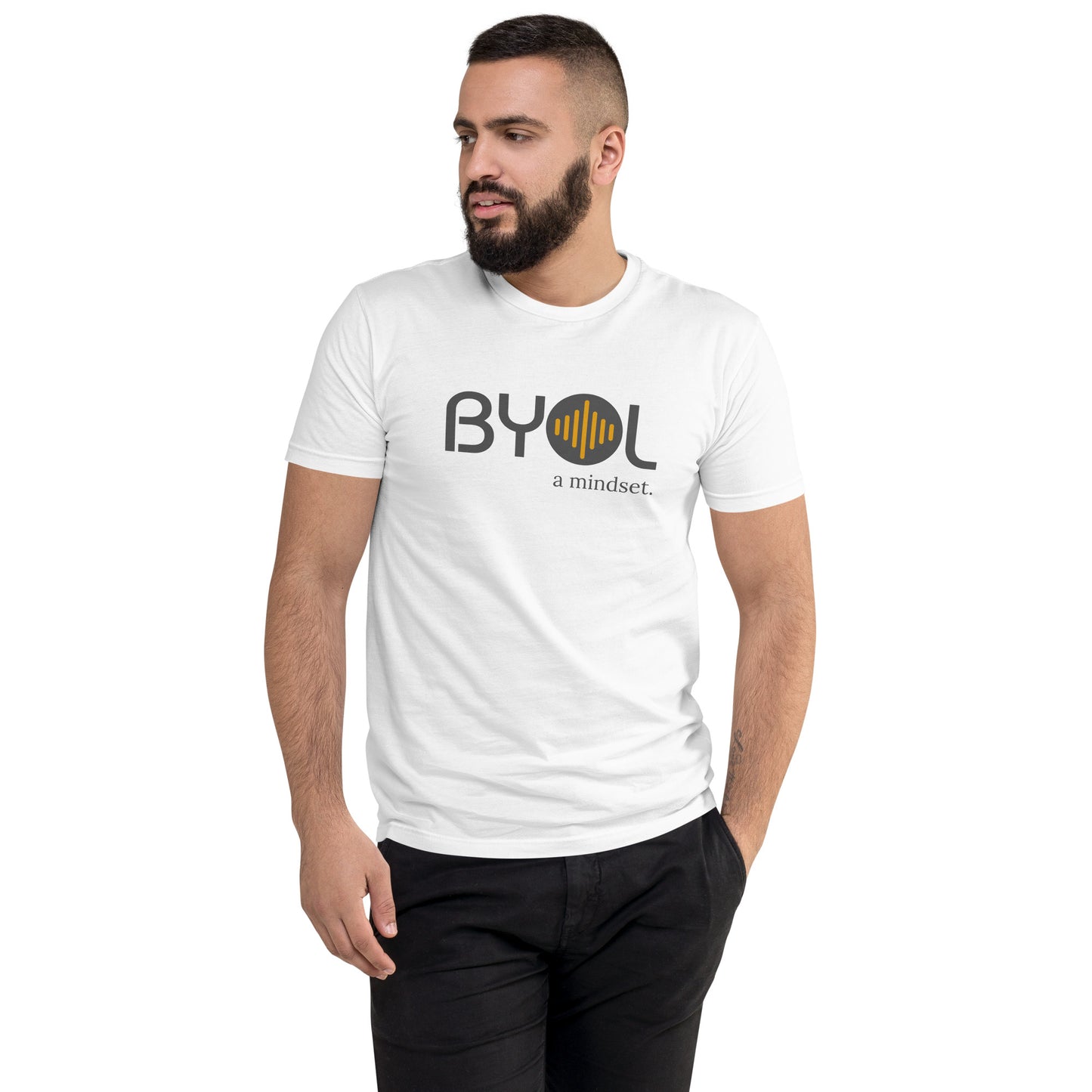 A young man with short dark hair and a beard wearing a white "BYOL: a mindset" T-shirt, standing with one hand in his pocket and looking to the side. The T-shirt features the "BYOL" logo in gray and yellow on the front and is available in multiple colors (red, blue, gray, plus more) and sizes (S-3XL). The "be you out loud" logo is displayed at the top.