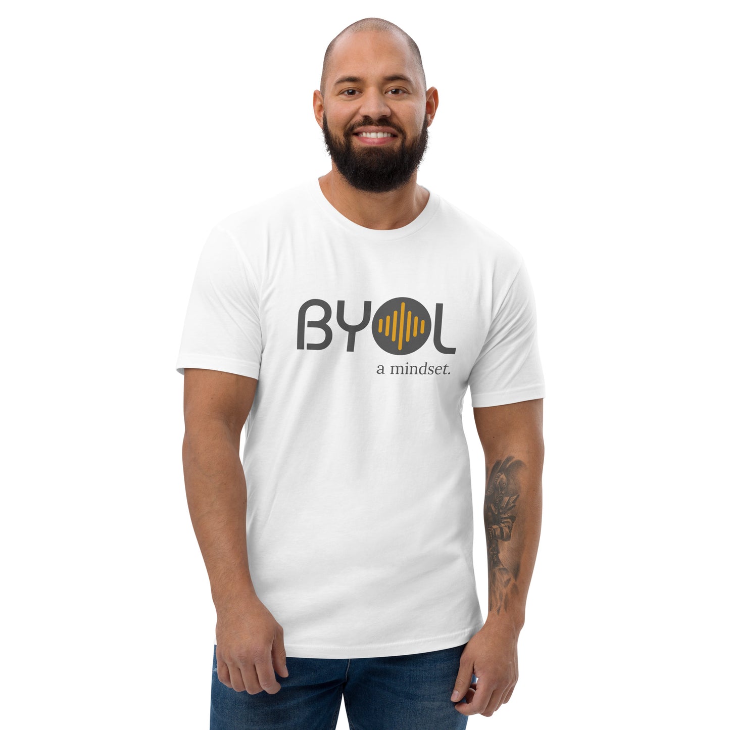 A bearded man with a shaved head wearing a white "BYOL: a mindset" T-shirt, smiling and standing with his arms at his sides. The T-shirt features the "BYOL" logo in gray and yellow on the front and is available in multiple colors (red, blue, gray, white, plus more) and sizes (S-3XL). The "be you out loud" logo is displayed at the top.