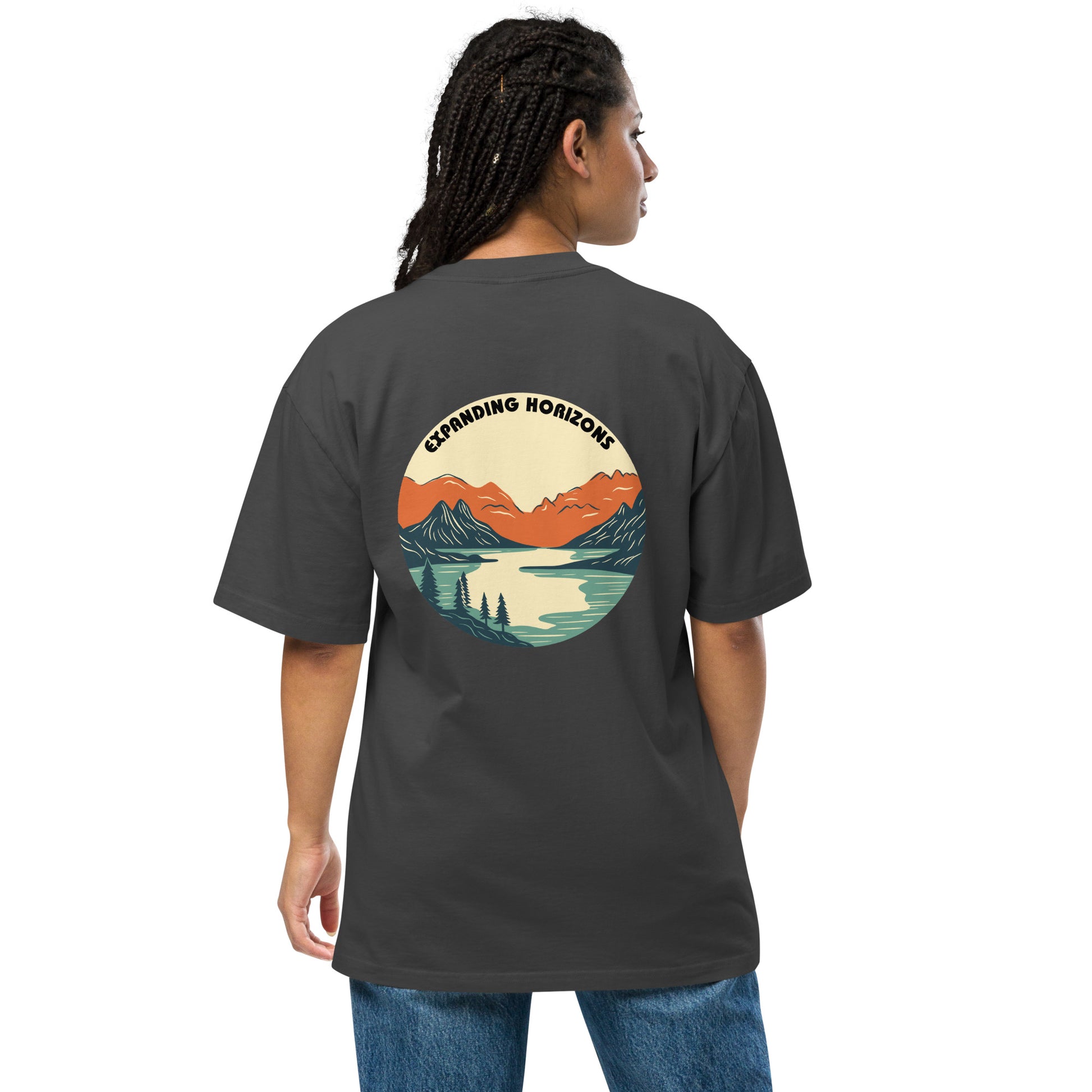 Woman wearing a faded black 'Expanding Horizons' Oversized Tee from Be You Out Loud, showcasing a scenic mountain and lake graphic in warm hues, signifying adventure and tranquility.