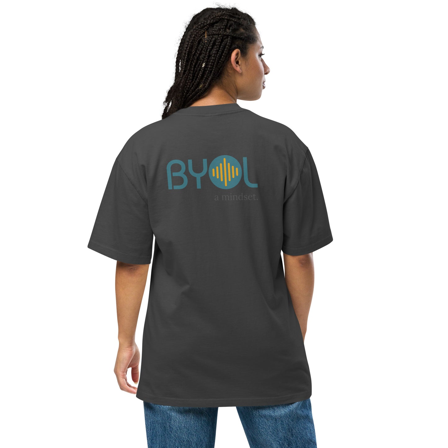 A young woman with long braids wearing a faded black "BYOL: a mindset" T-shirt, viewed from the back. The T-shirt features the "BYOL" logo in teal and yellow on the back and is available in multiple colors (dark gray, beige, light blue, white, plus more) and sizes (S-3XL). The "be you out loud" logo is displayed at the top.