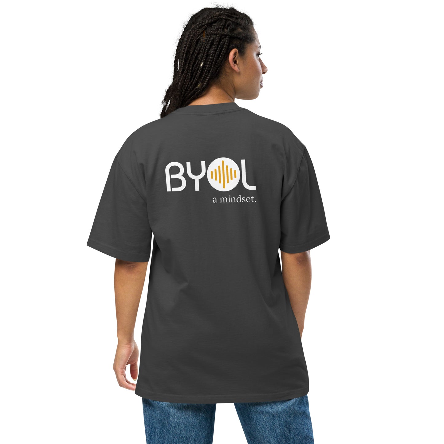 A young woman with long braids wearing a faded black "BYOL: a mindset" T-shirt, viewed from the back. The T-shirt features the "BYOL" logo in white and yellow on the back and is available in multiple colors (dark gray, beige, light blue, white, plus more) and sizes (S-3XL). The "be you out loud" logo is displayed at the top.