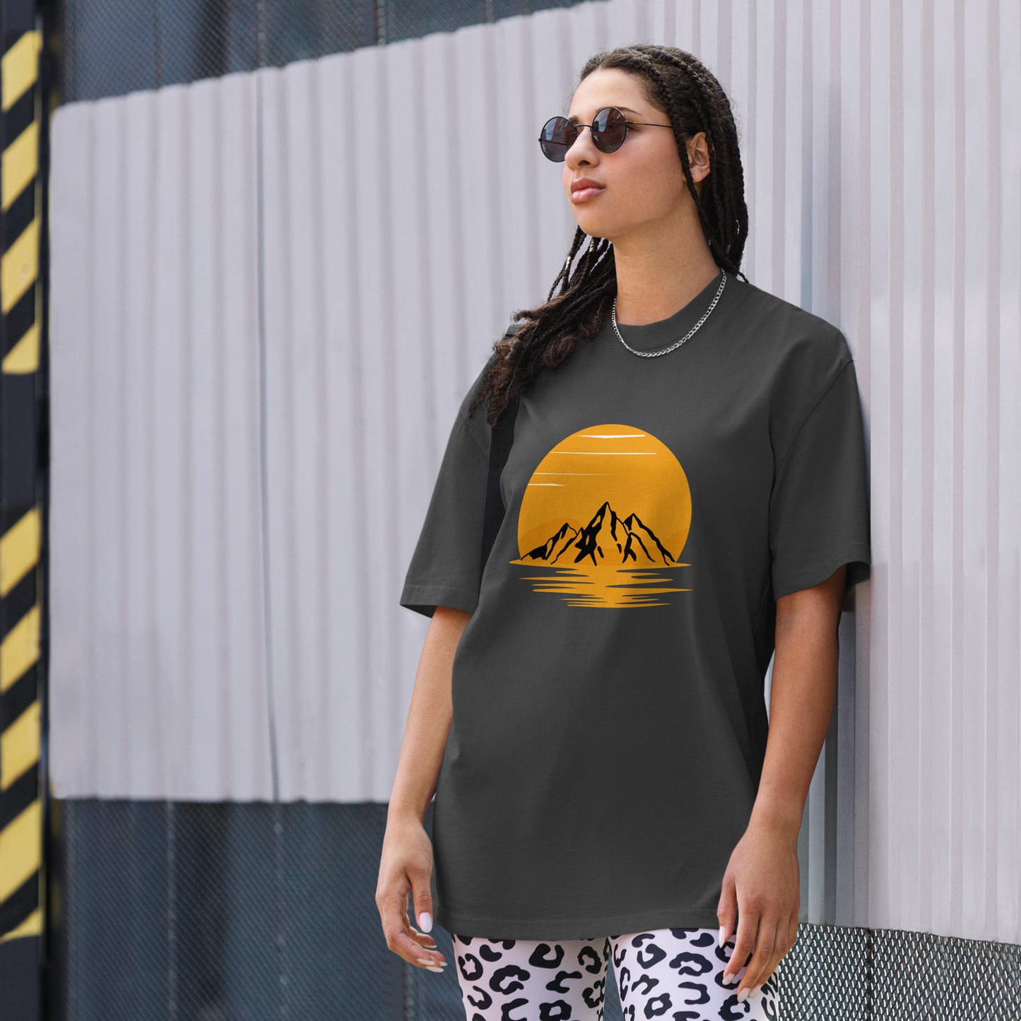 Fashion-forward woman in a Women's Sunset Mountains Lifestyle faded black Oversized Tee against an urban backdrop, echoing the adventure of Be You Out Loud.