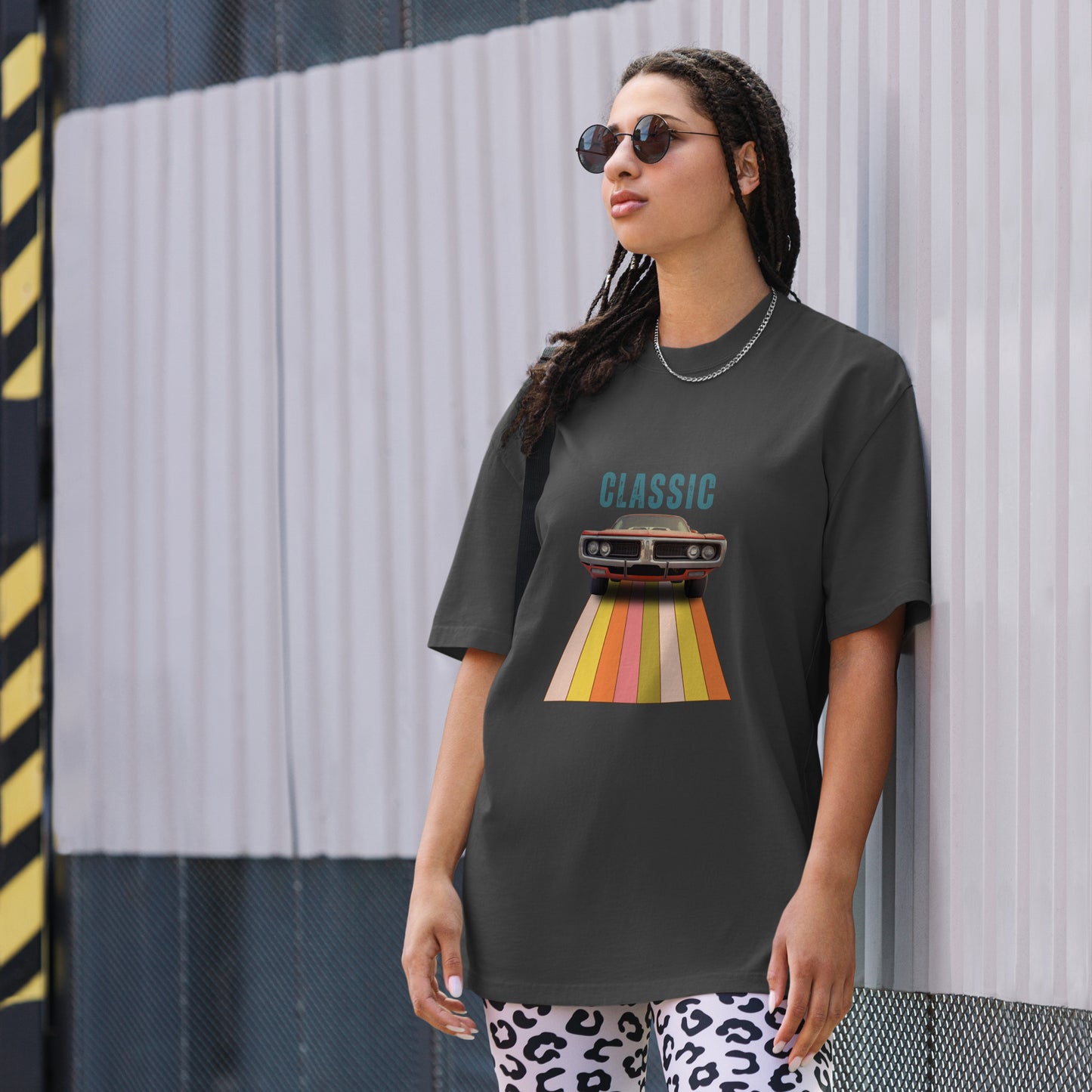 Cool and casual, a woman models a faded black 'CLASSIC' graphic tee featuring a vintage car cruising down a retro striped road, and paired with relaxed blue jeans and chic sunglasses.