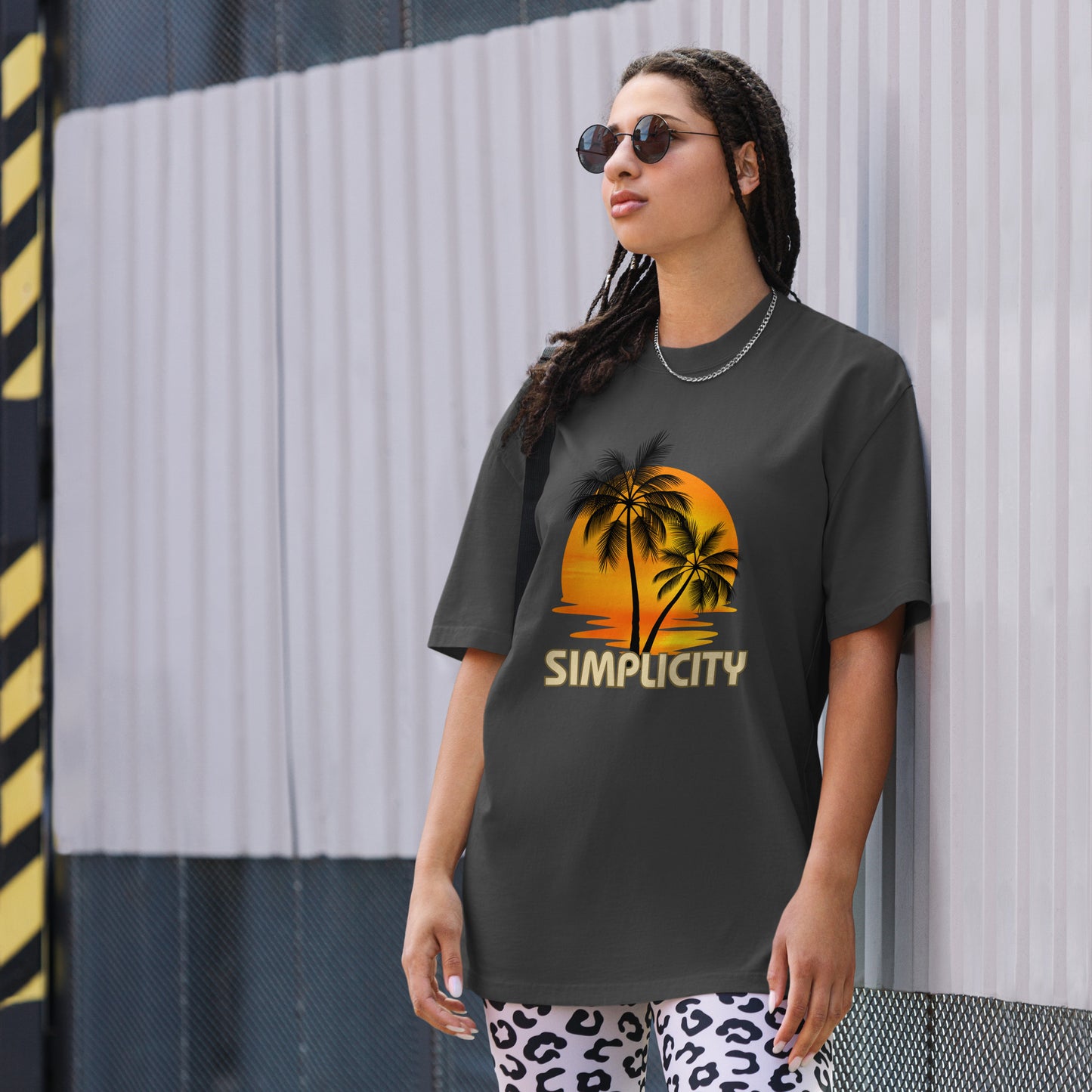 A woman in a Women's Sunset Simplicity faded black Oversized Tee with a minimalist palm design in soft earth tones, exuding calm and trendy vibes.