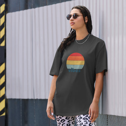 Confident woman showcasing a Women's 'vibes' faded black Oversized Tee with a retro-inspired sunset graphic, radiating laid-back, positive vibes in a neutral color, complemented by chic sunglasses. 