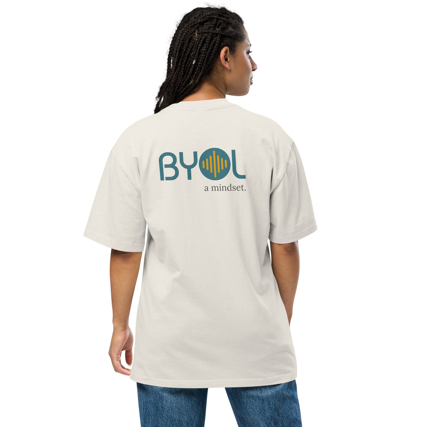 A young woman with long braids wearing a faded bobe "BYOL: a mindset" T-shirt, viewed from the back. The T-shirt features the "BYOL" logo in teal and yellow on the back and is available in multiple colors (dark gray, beige, light blue, white, plus more) and sizes (S-3XL). The "be you out loud" logo is displayed at the top.