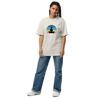 Woman in a relaxed pose wearing a faded bone 'Zen' graphic T-shirt with a tranquil sunset and silhouette design, available from size S to 3XL, styled with wide-leg blue jeans and white sneakers.