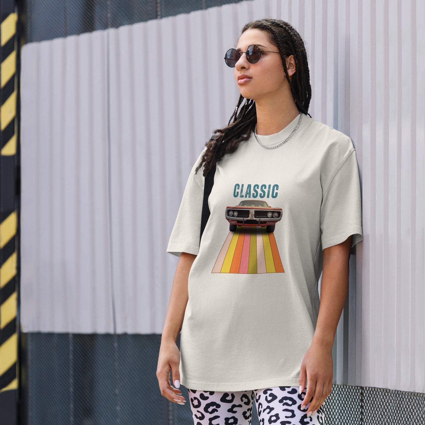 Cool and casual, a woman models a faded bone 'CLASSIC' graphic tee featuring a vintage car cruising down a retro striped road, and paired with relaxed blue jeans and chic sunglasses.