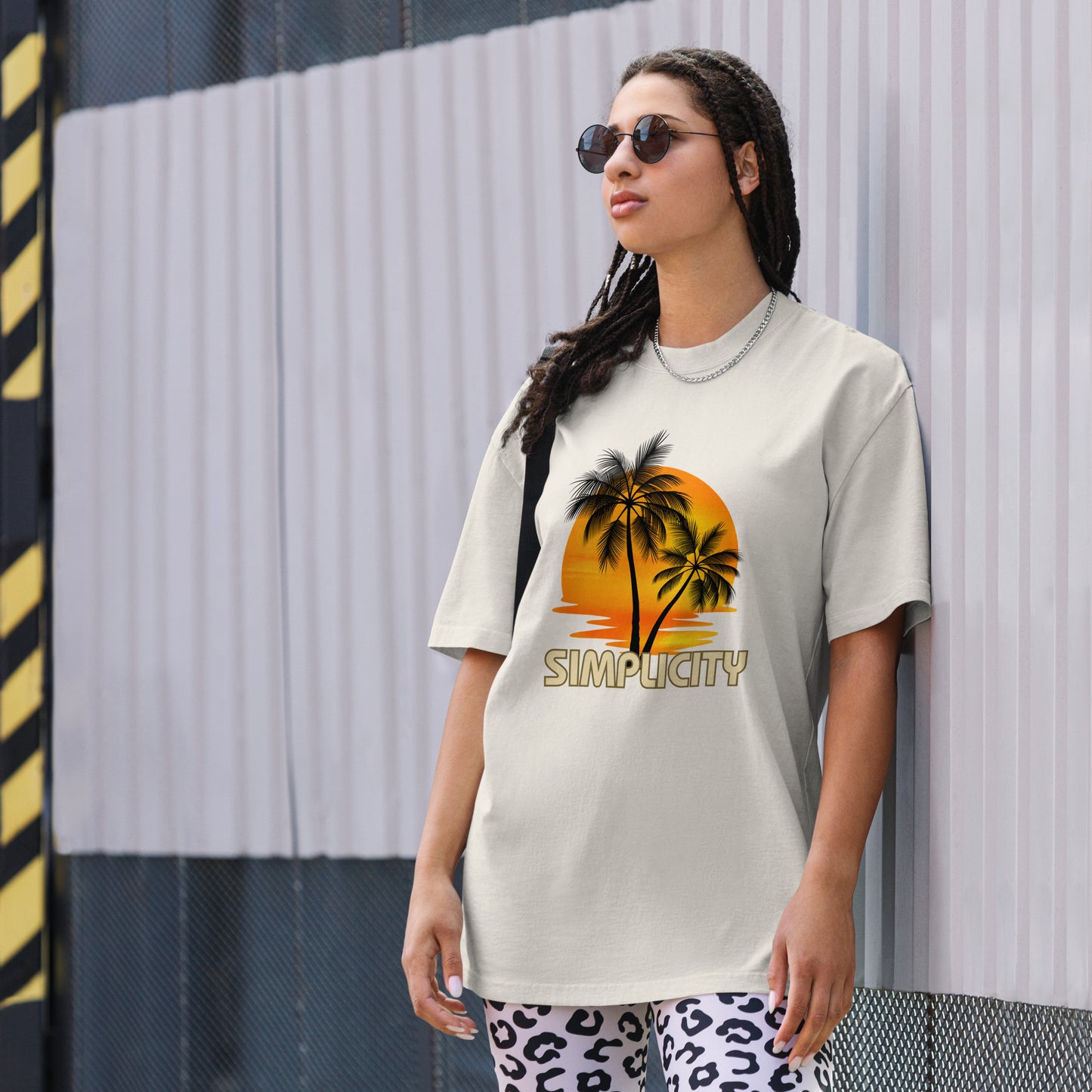 A woman in a Women's Sunset Simplicity faded bone Oversized Tee with a minimalist palm design in soft earth tones, exuding calm and trendy vibes.