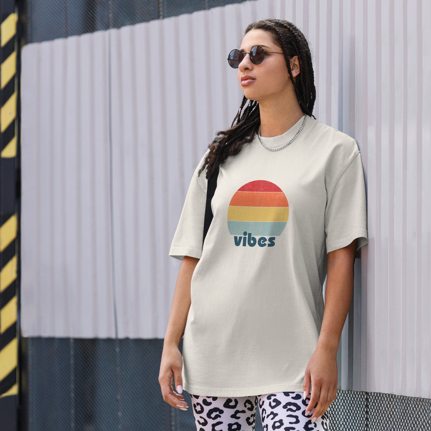 Confident woman showcasing a Women's 'vibes' faded bone Oversized Tee with a retro-inspired sunset graphic, radiating laid-back, positive vibes in a neutral color, complemented by chic sunglasses. 