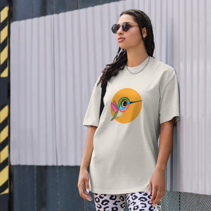 Woman models a faded bone Oversized Tee with a colorful hummingbird design on a yellow circle background, embodying a lively spirit.