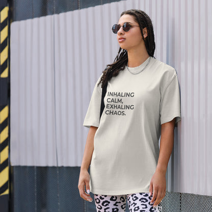 A woman wearing a faded bone "Inhaling calm, exhaling chaos" t-shirt, styled with leopard print leggings and sunglasses, leaning against a corrugated metal wall with a confident expression. The casual yet trendy outfit showcases self-expression and boldness. Perfect for promoting empowering fashion statements.