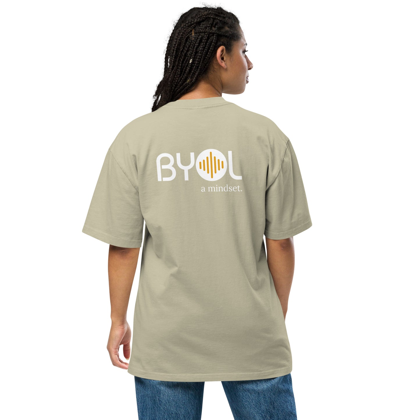 A young woman with long braids wearing a faded eucalyptus "BYOL: a mindset" T-shirt, viewed from the back. The T-shirt features the "BYOL" logo in white and yellow on the back and is available in multiple colors (dark gray, beige, light blue, white, plus more) and sizes (S-3XL). The "be you out loud" logo is displayed at the top.