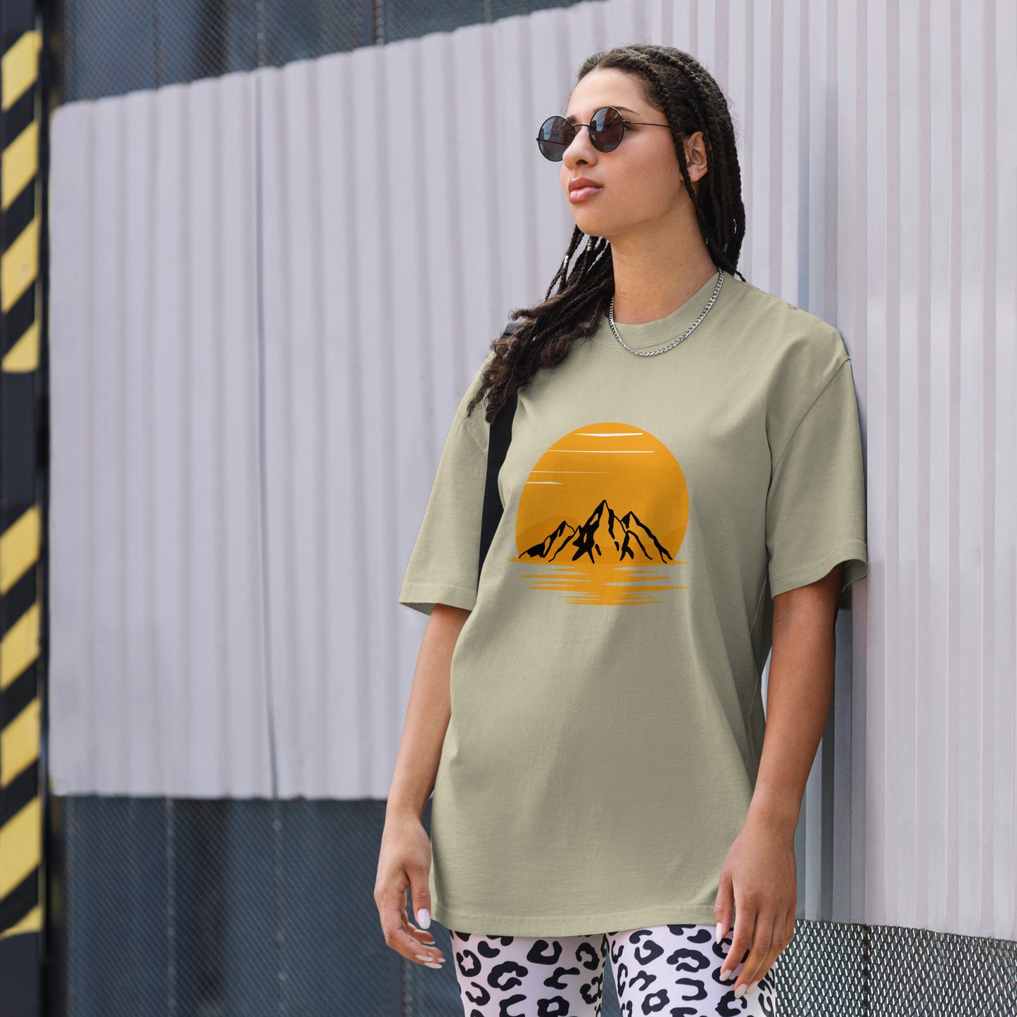 Fashion-forward woman in a Women's Sunset Mountains Lifestyle faded eucalyptus Oversized Tee against an urban backdrop, echoing the adventure of Be You Out Loud.